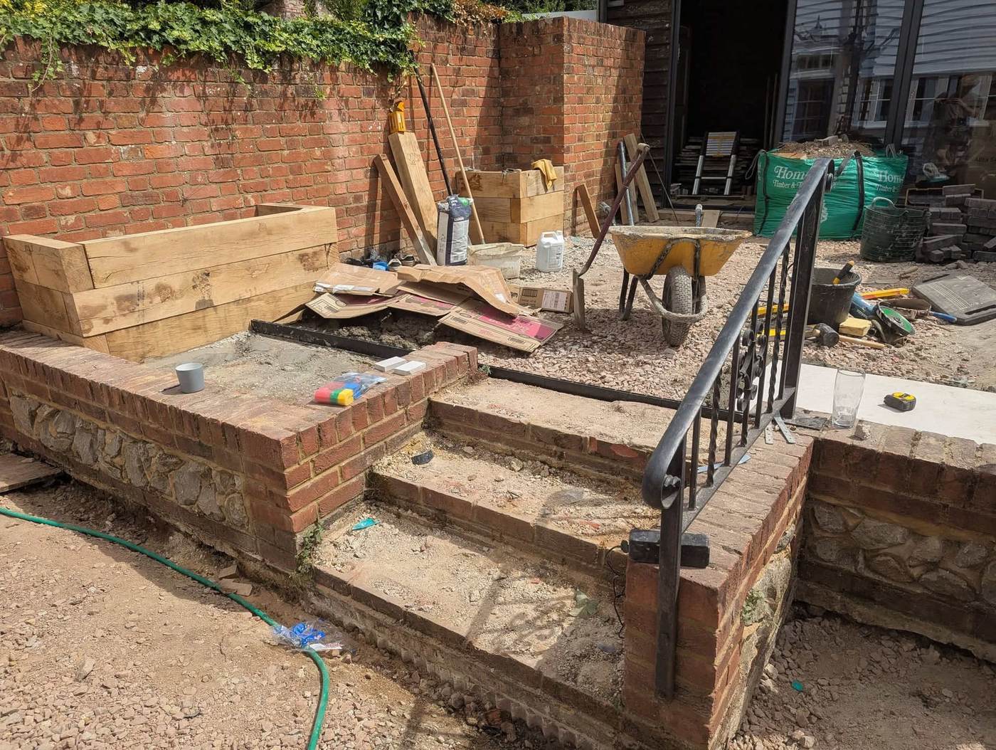 The walled garden stripped out: bare steps, gravel, a wheelbarrow and tools against the old brick walls